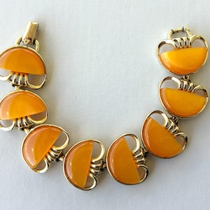 May include: Vintage gold-tone bracelet featuring orange resin half-circle shapes. The bracelet has a gold clasp and is composed of multiple linked segments. The orange resin has a glossy finish, and the bracelet is set against a white background.