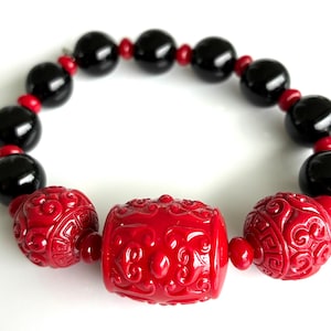 May include: A beaded bracelet featuring large, glossy black beads interspersed with smaller red beads. The bracelet includes three ornate red carved beads with intricate designs, adding a striking contrast to the black and red color scheme.