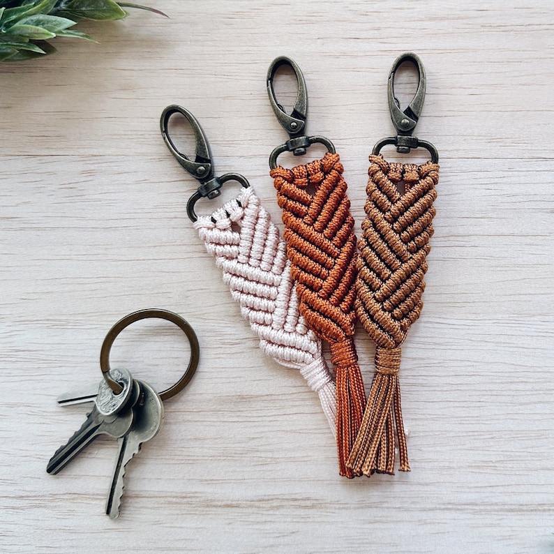 May include: Three keychains with a braided design in brown, light brown, and white. Each keychain has a silver metal ring and a tassel.
