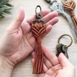 May include: A brown macrame keychain with a tassel and a silver metal clasp.
