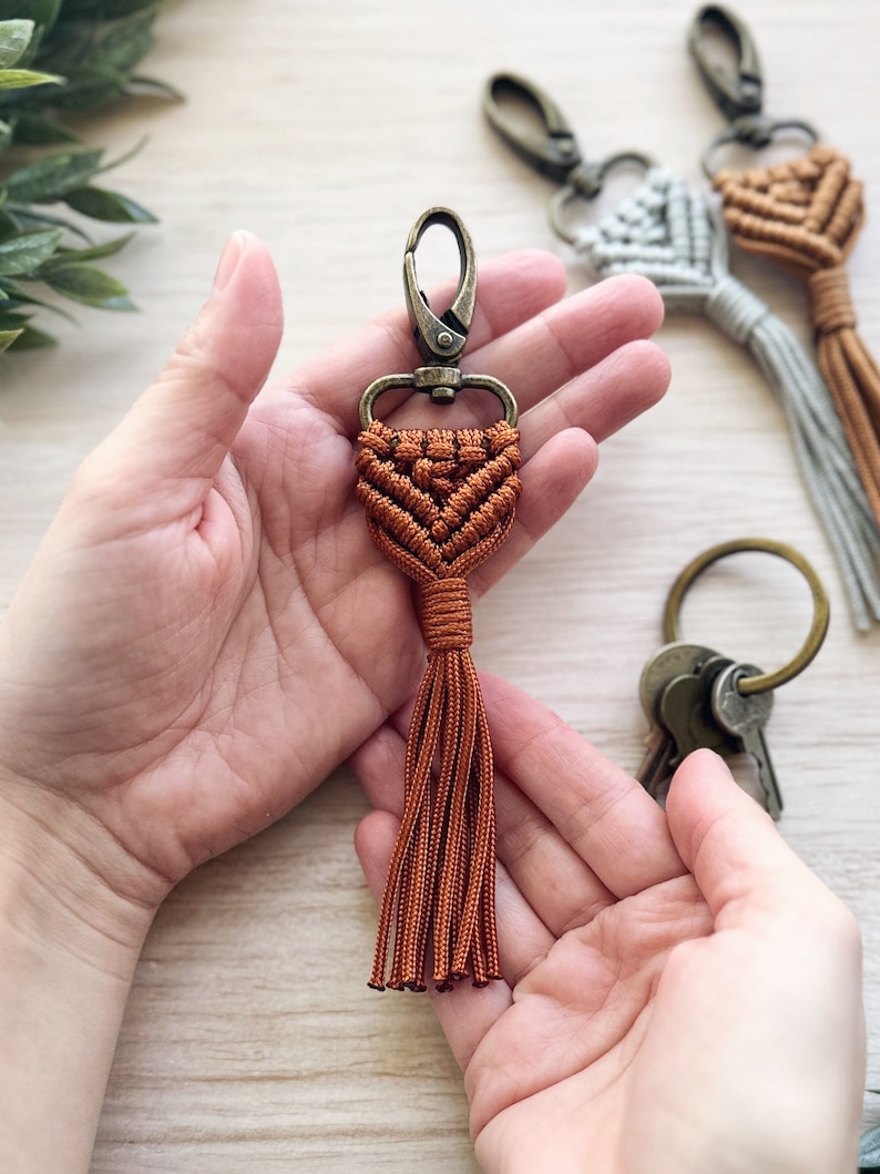 May include: A brown macrame keychain with a tassel and a silver metal clasp.