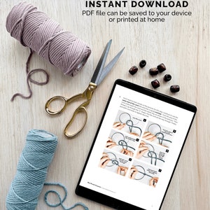 K&ouml;nnte beinhalten: Ein digitales Tablet zeigt ein PDF-Muster f&uuml;r ein Makramee-Projekt. Das Muster enth&auml;lt Anweisungen und Illustrationen zum Erstellen eines Makramee-Knotens. Zwei Garnrollen, eine rosa und eine blaue, sind neben dem Tablet zu sehen, zusammen mit einer goldenen Schere. Der Text auf dem Tablet lautet "PATTERN IS AN INSTANT DOWNLOAD PDF file can be saved to your device or printed at home".