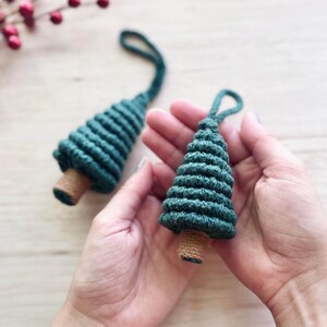 May include: Two green, crocheted Christmas tree ornaments with brown bases. The ornaments are held in the palms of two hands.
