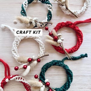 May include: Craft kit with five small wreaths made of white, red, and green yarn. Each wreath is decorated with dried flowers and berries.
