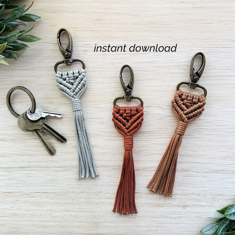 May include: Three macrame keychains with tassels. The keychains are in grey, brown, and orange. The keychains are attached to silver key rings.
