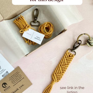 May include: A yellow paracord keychain with a chevron pattern and a tassel. The keychain is in a box with a spool of yellow paracord and a metal clasp. The text "full DIY kits also available for this design" is at the top of the image. The text "materials nylon paracord" is on a small brown card in the box. The text "see link in the listing description" is at the bottom of the image.