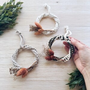 K&ouml;nnte beinhalten: Drei kleine Makramee-Kr&auml;nze mit getrockneten Blumen und Gr&uuml;n. Die Kr&auml;nze sind aus nat&uuml;rlichem Baumwollseil gefertigt und haben einen rustikalen, bohemischen Stil.