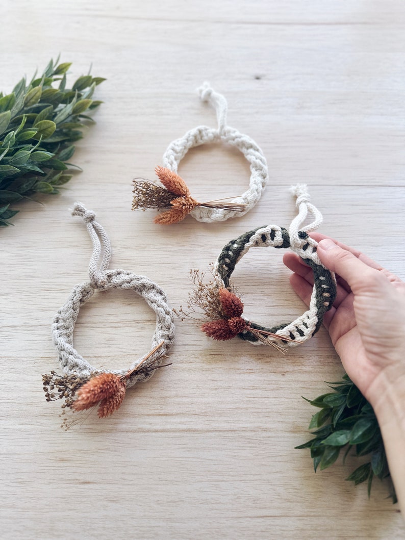 K&ouml;nnte beinhalten: Drei kleine Makramee-Kr&auml;nze mit getrockneten Blumen und Gr&uuml;n. Die Kr&auml;nze sind aus nat&uuml;rlichem Baumwollseil gefertigt und haben einen rustikalen, bohemischen Stil.