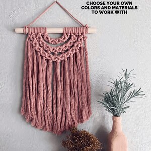 May include: A dusty rose macrame wall hanging with a wooden dowel and hanging cord. The macrame features a half-circle design with long fringe. Text reads: FINISHED PATTERN RESULTS. CHOOSE YOUR OWN COLORS AND MATERIALS TO WORK WITH.