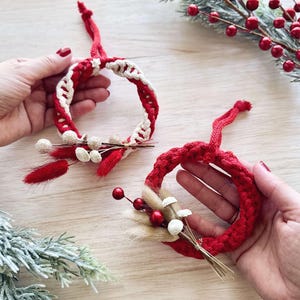 K&ouml;nnte beinhalten: Zwei rot-wei&szlig;e geh&auml;kelte Weihnachtsornamente mit getrockneten Blumenakzenten. Die Ornamente sind handgefertigt und haben ein schlichtes, elegantes Design.