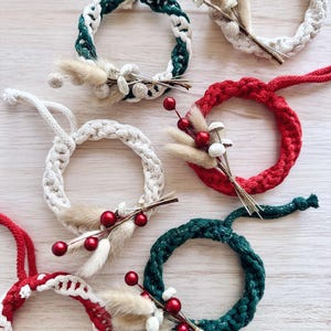 K&ouml;nnte beinhalten: Sechs handgefertigte Weihnachtskr&auml;nze in verschiedenen Farben, darunter Gr&uuml;n, Rot und Wei&szlig;. Jeder Kranz ist mit getrockneten Blumen und Beeren verziert.