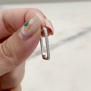 Könnte beinhalten: Ein silberner Creolenohrring mit einer Reihe kleiner, klarer Zirkonia-Steine.