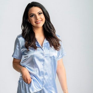 May include: A light blue satin pajama set with short sleeves and shorts. The top has a button-up front and a pocket on the left side.