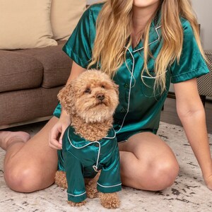 K&ouml;nnte beinhalten: Ein passendes Set aus smaragdgr&uuml;nem Satin-Pyjama mit wei&szlig;er Paspelierung. Das Set besteht aus einem kurz&auml;rmeligen, gekn&ouml;pften Oberteil f&uuml;r Menschen und einem lang&auml;rmeligen, gekn&ouml;pften Oberteil f&uuml;r einen kleinen Hund, beide mit klassischem Reverskragen.