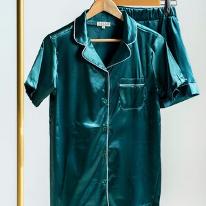 K&ouml;nnte beinhalten: Ein dunkel-smaragdgr&uuml;nes Pyjama-Set, bestehend aus einem kurz&auml;rmeligen Hemd mit Knopfleiste, Reverskragen und Brusttasche sowie einer passenden Shorts. Das Set ist mit einer wei&szlig;en Paspelierung am Kragen, der Tasche und der Knopfleiste versehen.