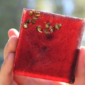 May include: A square, red, translucent bar of soap with dried flowers embedded inside.