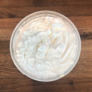 May include: A close-up of a clear glass cup filled with whipped cream. The whipped cream is piled high and has a fluffy texture.