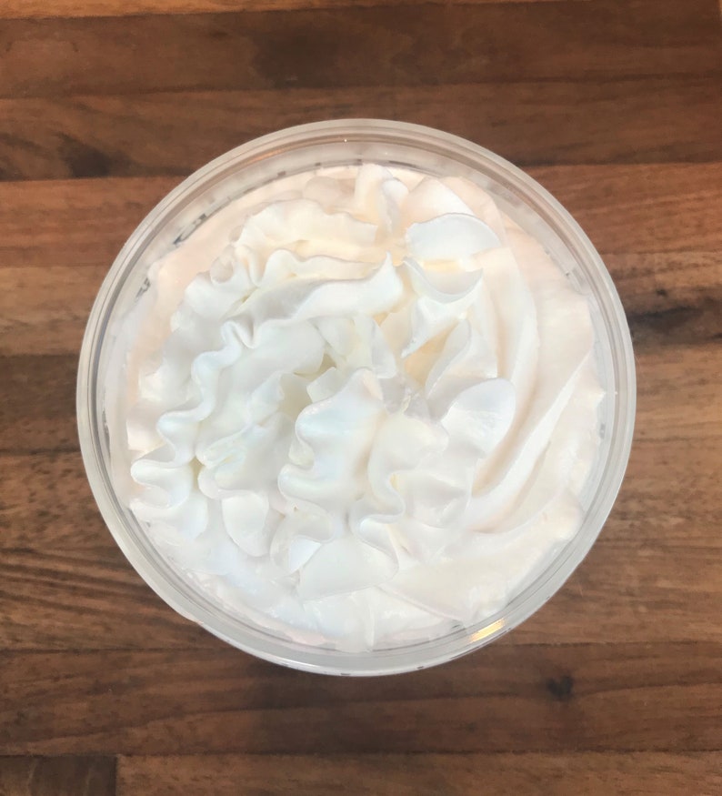 May include: A close-up of a clear glass cup filled with whipped cream. The whipped cream is piled high and has a fluffy texture.