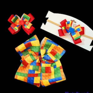 May include: A set of three hair bows featuring a colorful Lego brick pattern. The bows are made of red, yellow, green, blue, and orange ribbon. The largest bow is a large, double-looped bow. The medium bow is a single-looped bow. The smallest bow is a single-looped bow attached to a headband.
