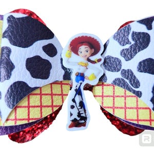 May include: A red, white, and black cow print bow with a yellow and red checkered pattern and a character from the Toy Story movie, Woody, in the center.