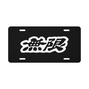 May include: A rectangular black license plate featuring the white Japanese kanji characters for "Mugen" in the center. The plate has four mounting slots, two at the top and two at the bottom, and a solid black background surrounding the white text.