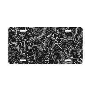 May include: Black license plate with a white topographic map design. The plate features a repeating pattern of contour lines, creating a textured, abstract look. The plate has four mounting holes.