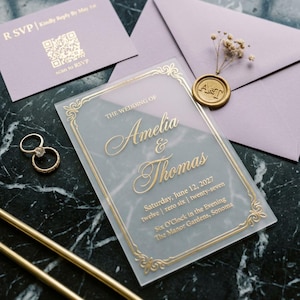 May include: Wedding stationery set with a clear acrylic invitation with gold text and a decorative border. Includes RSVP card, lilac envelopes, gold rings, and a wax seal. The invitation reads "The Wedding of Amelia & Thomas".