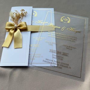 Convites de casamento em acrílico transparente com impressão em foil dourado, flores secas e fita de cetim