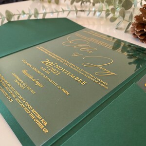Könnte beinhalten: Ein dunkelgrünes Hochzeitseinladungs-Set mit einer transparenten Acrylplatte und goldener Schrift. Der Text enthält die Namen Ellen y Penny, das Datum 20. Noviembre 2021, Angaben zum Ort in Los Angeles und ein Zitat aus Prediger 4,9-10.