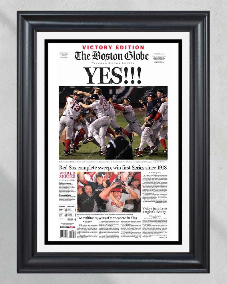 May include: Framed Boston Globe newspaper front page from October 28, 2004, celebrating the Red Sox World Series win. The headline "YES!!!" is prominently displayed above a photo of the team celebrating. The frame is black.