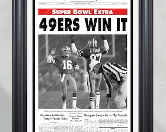 May include: Framed black and white print of the San Francisco Chronicle newspaper from January 21, 1985, with the headline "49ERS WIN IT." The image shows football players celebrating a Super Bowl victory. The frame is black.