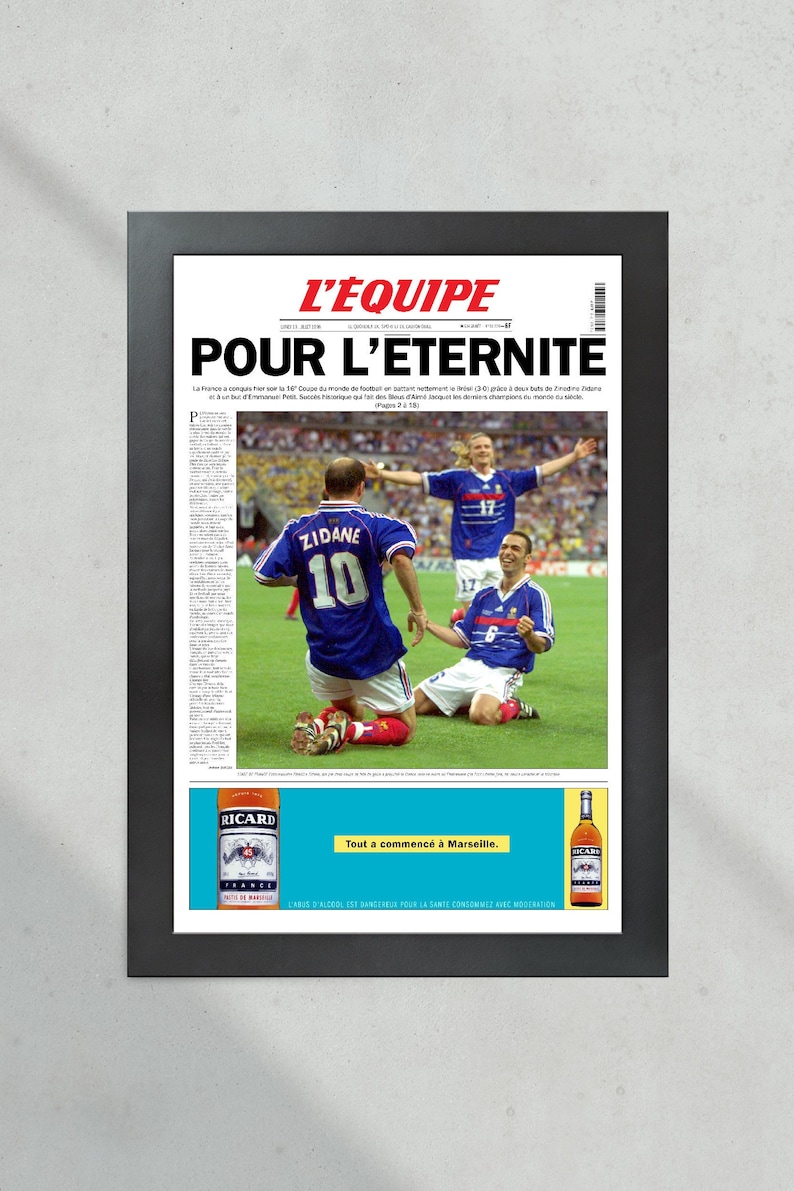 May include: A vintage newspaper clipping from L'Equipe, a French sports newspaper, with the headline "Pour l'Eternite" (For Eternity). The image shows French soccer players Zinedine Zidane and Emmanuel Petit celebrating their victory in the 1998 World Cup final. The newspaper is framed in black and features a Ricard ad at the bottom.