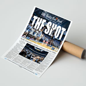May include: A newspaper print titled "The Shot" featuring a basketball game image. The headline reads "The Daily Tar Heel". The article highlights Seth Trimble's game-winning shot against Duke. The print is rolled up with a brown cardboard tube.