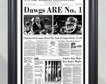 May include: A black and white newspaper clipping from The Atlanta Constitution, dated January 2, 1981, with the headline "Dawgs ARE No. 1". The article reports on the University of Georgia Bulldogs' victory over Notre Dame in the Sugar Bowl. The headline is in bold, large font, and the article is surrounded by smaller articles about other news events.