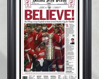 Op de afbeelding: Een ingelijste voorpagina van de Detroit Free Press met de kop "BELIEVE!" in rode letters. De afbeelding toont de Red Wings die hun Stanley Cup-overwinning vieren. De lijst is zwart.
