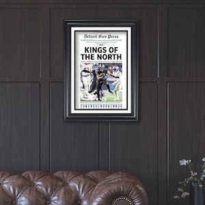 May include: Framed newspaper print with the headline "KINGS OF THE NORTH" from the Detroit Free Press. The print features a football game image. The frame is black, and the print is displayed on a dark wood-paneled wall.