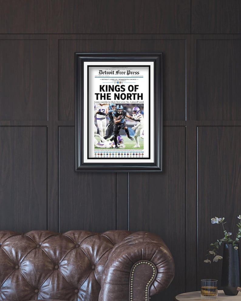 May include: Framed newspaper print with the headline "KINGS OF THE NORTH" from the Detroit Free Press. The print features a football game image. The frame is black, and the print is displayed on a dark wood-paneled wall.