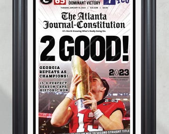 May include: A newspaper headline reads "2 GOOD!" with a photo of a football player holding up a trophy. The headline also reads "Georgia Repeats as Champions!" and "Dawgs Roll Over TCU on Way to Second Straight Title". The newspaper is titled "The Atlanta Journal-Constitution".