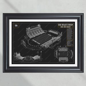 May include: Framed blueprint-style print of Kidd Brewer Stadium in Boone, North Carolina. The black and white architectural drawing shows the stadium's layout, including the field and seating areas. The print is in a black frame.