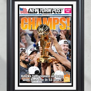 Op de afbeelding: Een ingelijste voorpagina van de New York Post met de titel CHAMPS! en een foto van basketballers die een gouden trofee omhoog houden. De kop luidt Knicks fans rejoice as team wins first title in 53 years met een kleine Amerikaanse vlag.