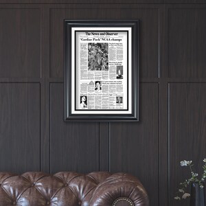 May include: A framed black and white newspaper clipping from The News and Observer, dated March 30, 1983, with the headline "Cardiac Pack' NCAA champs".