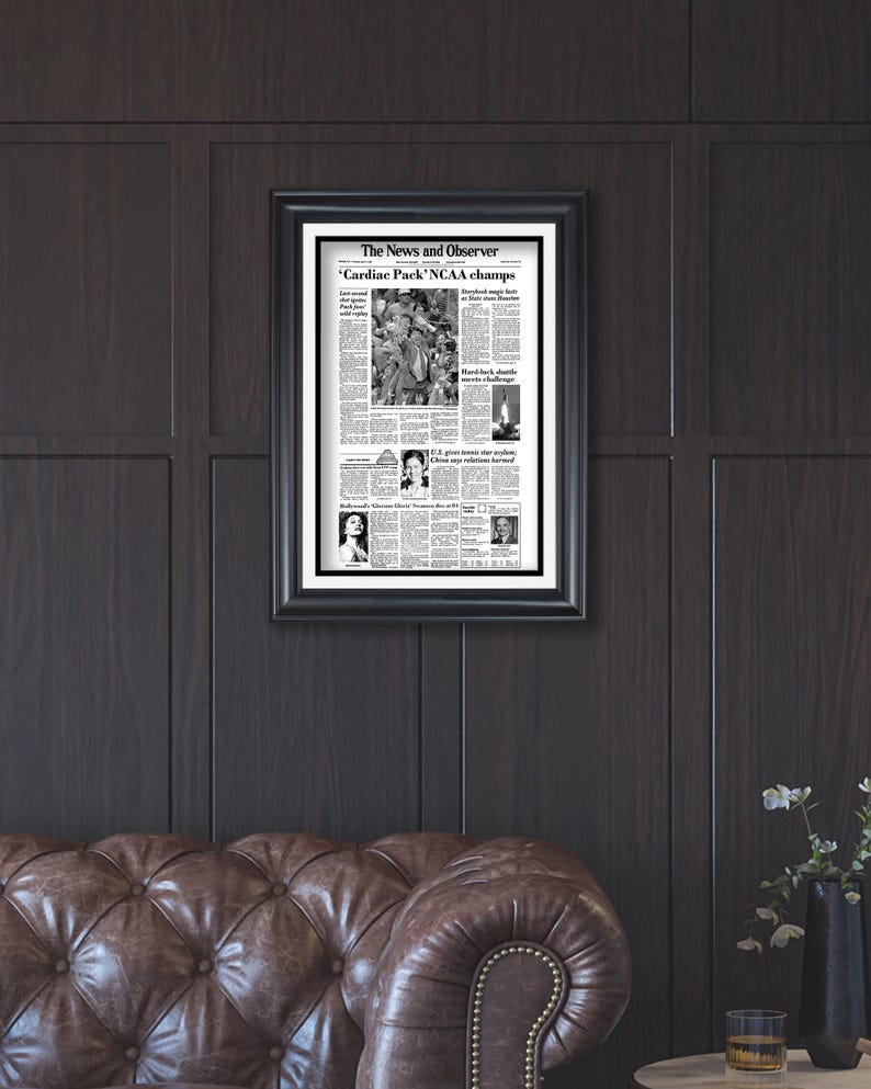 May include: A framed black and white newspaper clipping from The News and Observer, dated March 30, 1983, with the headline "Cardiac Pack' NCAA champs".