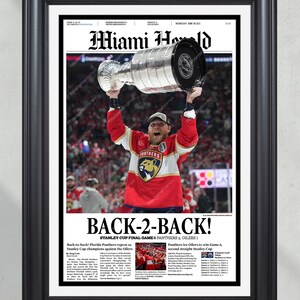 May include: Framed Miami Herald newspaper print celebrating the Florida Panthers' Stanley Cup victory. The headline reads "BACK-2-BACK!" with a photo of a player holding the Stanley Cup. The frame is black.