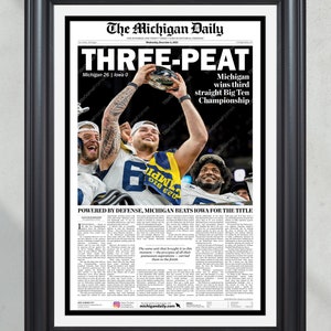 May include: A front page from The Michigan Daily newspaper, dated 4 December 2022, with the headline "THREE-PEAT" and the subheadline "Michigan wins third straight Big Ten Championship". The main image shows a football player holding up a trophy with teammates celebrating around him. The article headline reads "POWERED BY DEFENSE, MICHIGAN BEATS IOWA FOR THE TITLE".