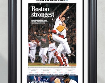 May include: A newspaper headline reads "Boston strongest" with a photo of two baseball players celebrating a win. The headline says "Red Sox finish what they started, defeat Cardinals for their eighth title." The newspaper is framed in a black frame.
