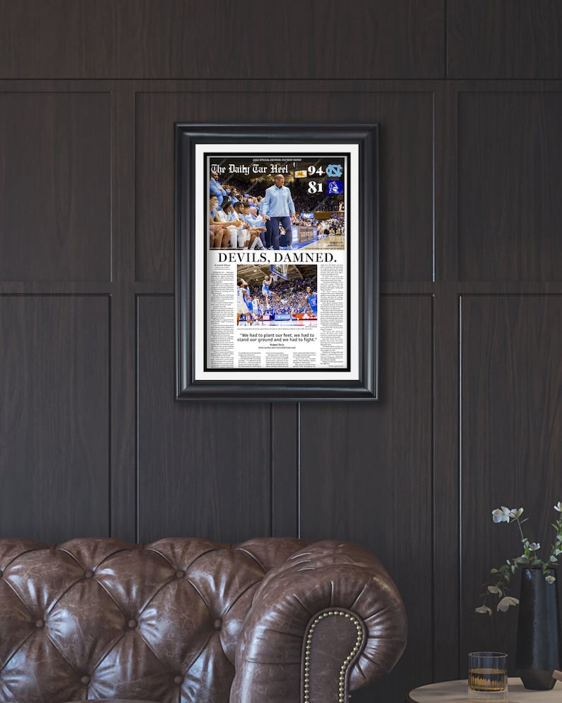 Puede incluir: Una impresi&oacute;n de peri&oacute;dico enmarcada de un partido de baloncesto con el titular "DEVILS, DAMNED." La impresi&oacute;n presenta una foto del partido con el marcador 94 a 81. El peri&oacute;dico se llama "The Daily Tar Heel."