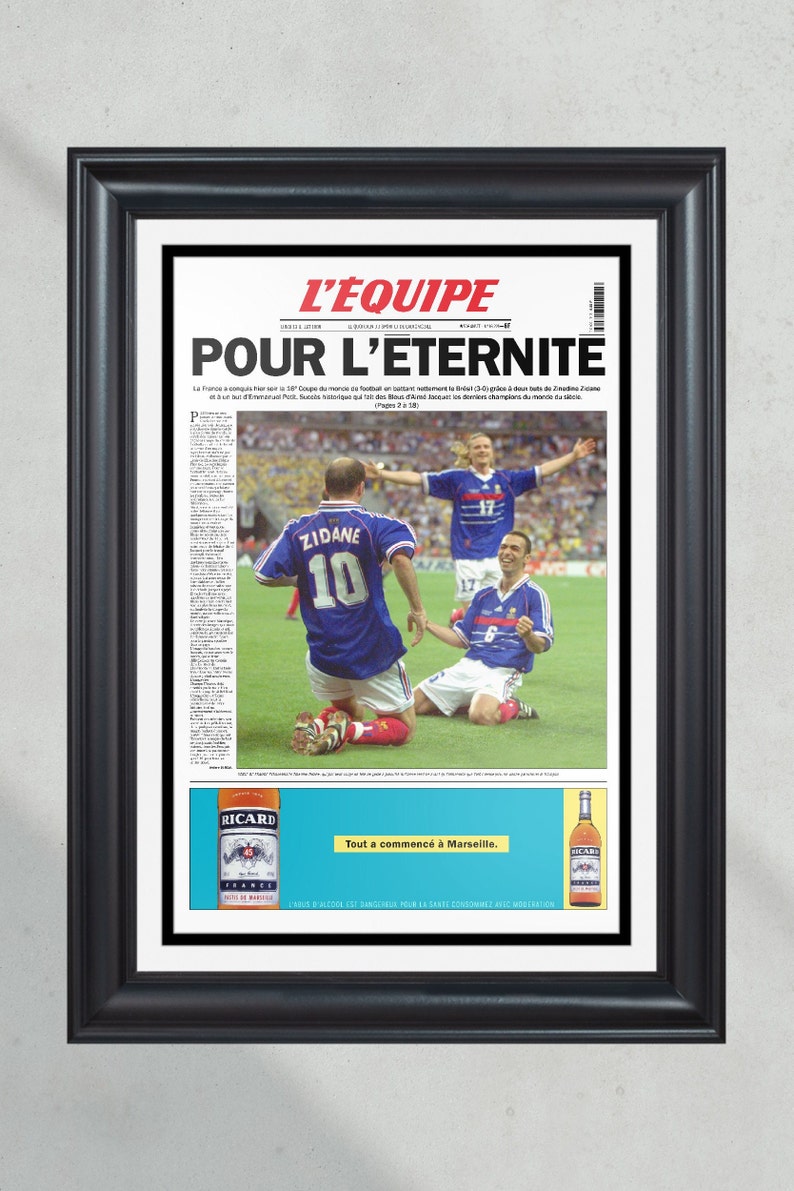 May include: A black and white newspaper front page with the headline "L'Equipe Pour L'Eternite" featuring a photo of French soccer players celebrating a victory. The text "Tout a commenc&eacute; &agrave; Marseille." is printed at the bottom of the page.
