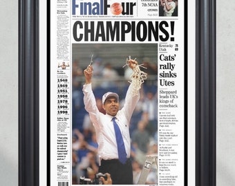 May include: A black and white newspaper front page with the headline "Final Four Champions!"  The headline is in large, bold, white letters. The newspaper is from the Lexington Herald-Leader and features a photo of a man in a white shirt and blue tie holding up a basketball net. The text on the newspaper reads "Kentucky 78 Utah 69 Cats' rally sinks Utes Sheppard leads UK's kings of comeback".