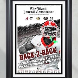 May include: Framed print of The Atlanta Journal-Constitution newspaper. The headline reads "BACK-2-BACK DAWGS ROLL OVER TIDE FOR SECOND STRAIGHT SEC TITLE." The image features a football player in a red helmet and jersey. The score is A 07, G 28.