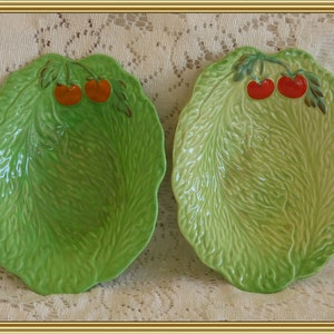 May include: Two green ceramic salad bowls shaped like lettuce leaves with red tomato accents.